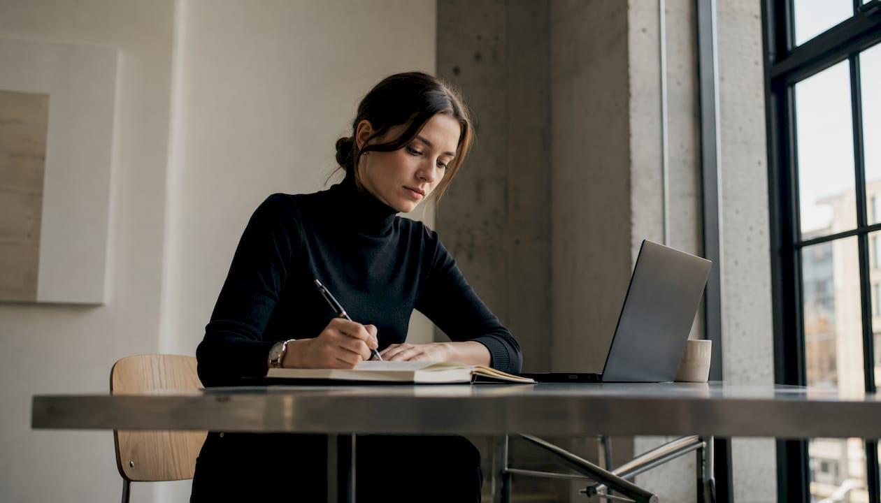 Eine Frau sitzt an ihrem Schreibtisch im Homeoffice und plant ihren Arbeitstag in Zeitblöcken.